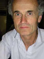 Julian Bell Artist: a man looking intently at the camera wearing a white open necked shirt